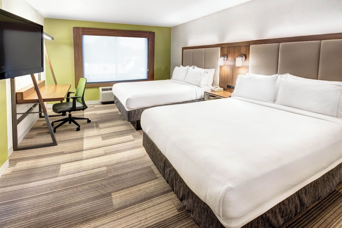 Habitación de hotel con dos camas, un escritorio con silla, televisor y ventana con vistas.