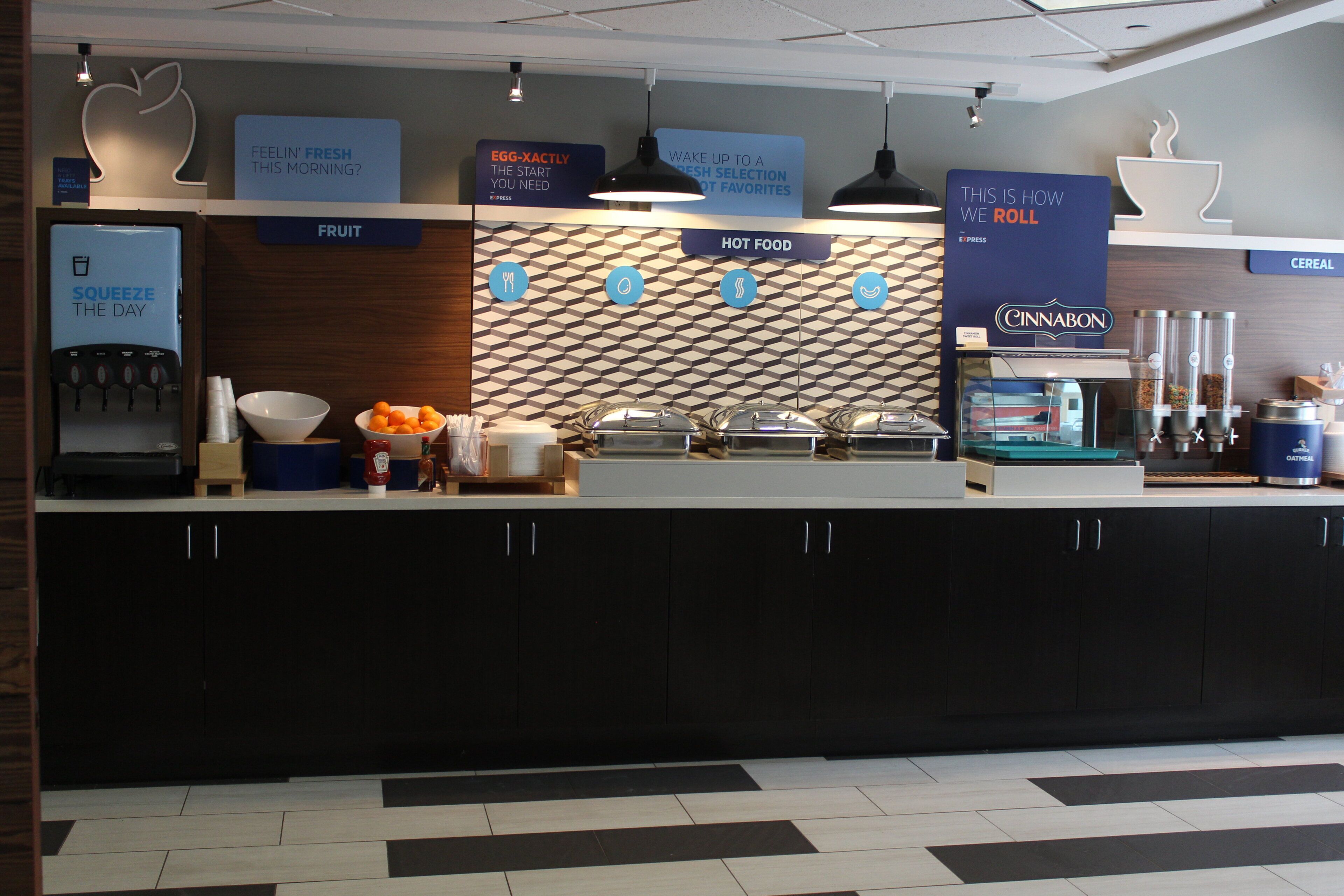 A breakfast bar with labeled sections for fruit, hot food, and cereal, including a cinnamon roll option.