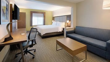 A hotel room with a bed, a desk, a chair, a sofa, and a TV.