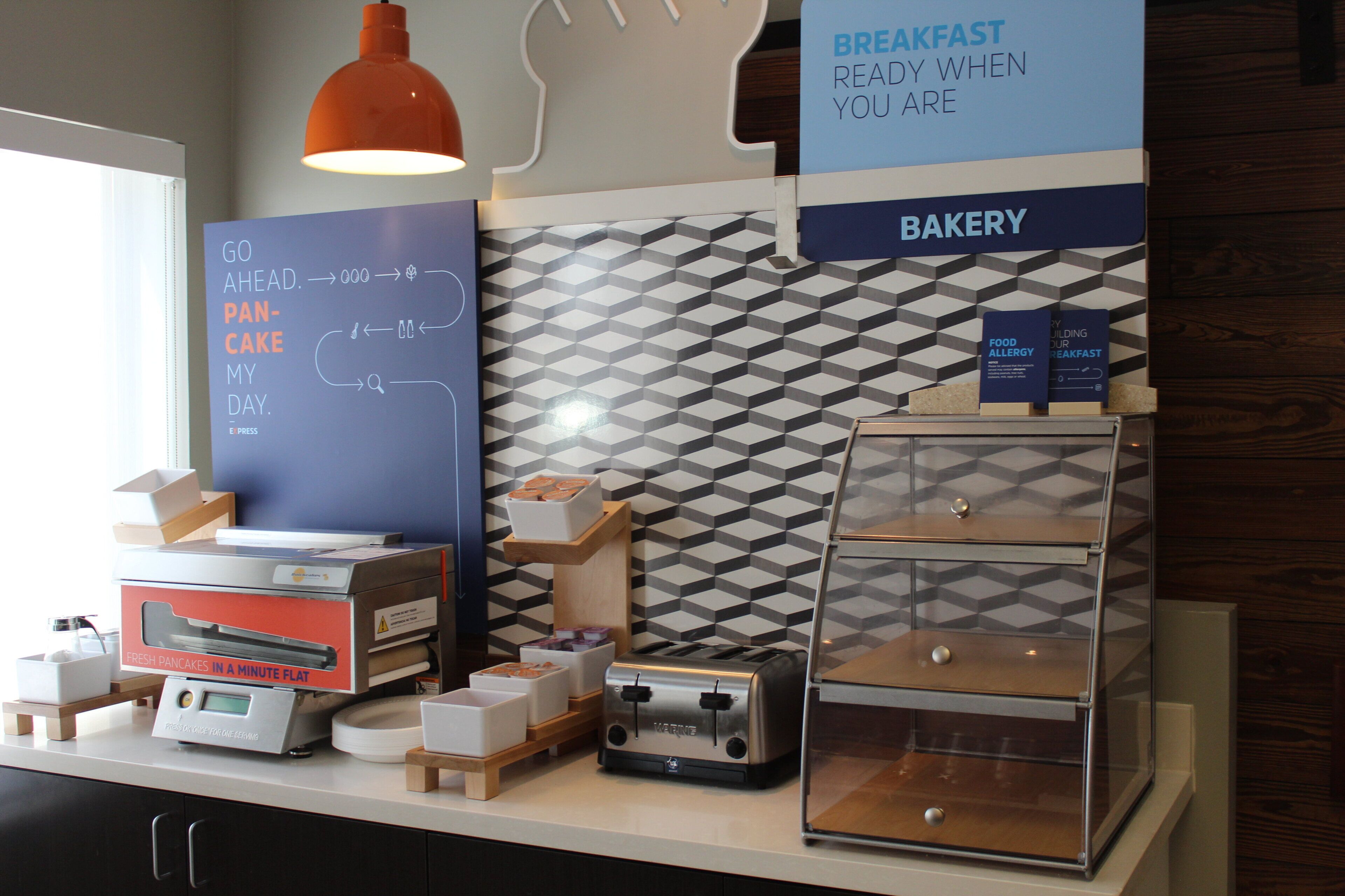 A breakfast area with a sign indicating it's ready when you are, a bakery section, and a waffle maker on the counter.