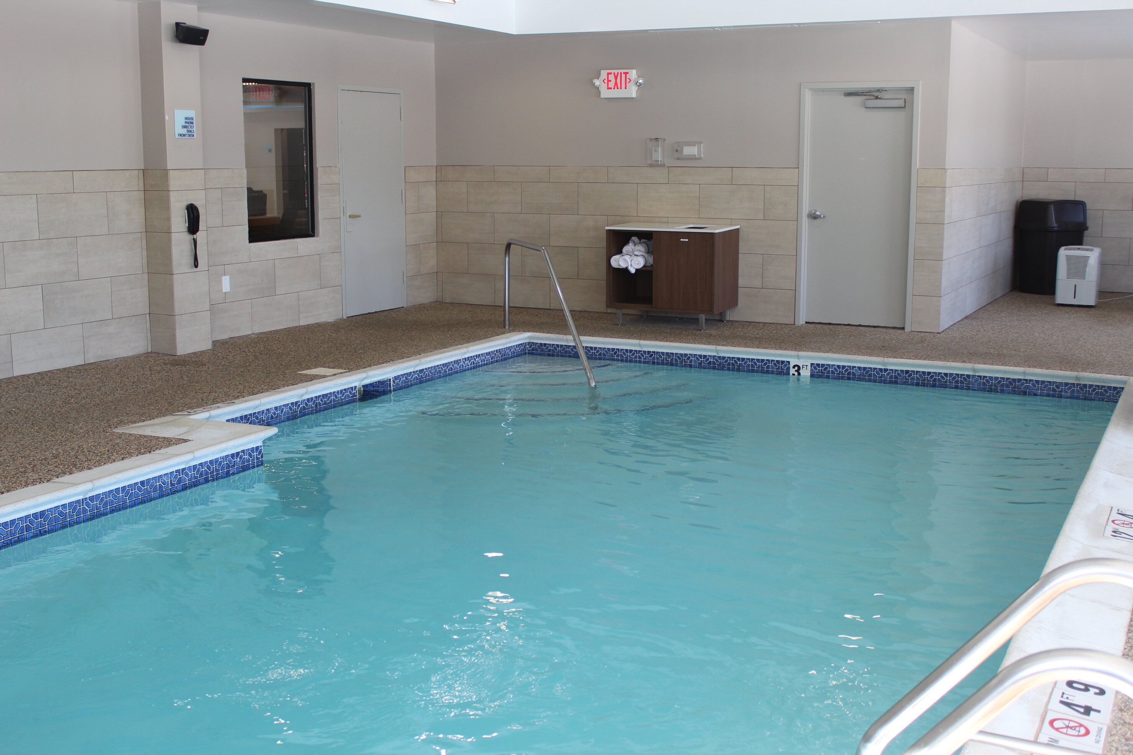 An indoor swimming pool with a clear water surface, a pool ladder, and a towel rack.