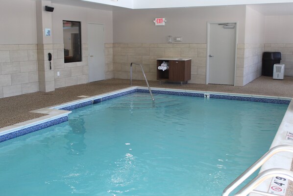 Una piscina interior con superficie de agua cristalina, una escalera de piscina y un perchero.