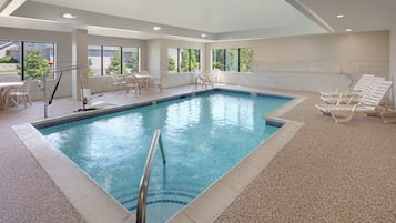 An indoor swimming pool with clear water, surrounded by lounge chairs and a table with chairs.