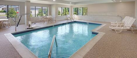 Una piscina interior con agua cristalina, rodeada de sillones de descanso y una mesa con sillas.