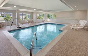 An indoor swimming pool with clear water, surrounded by lounge chairs and a table with chairs.