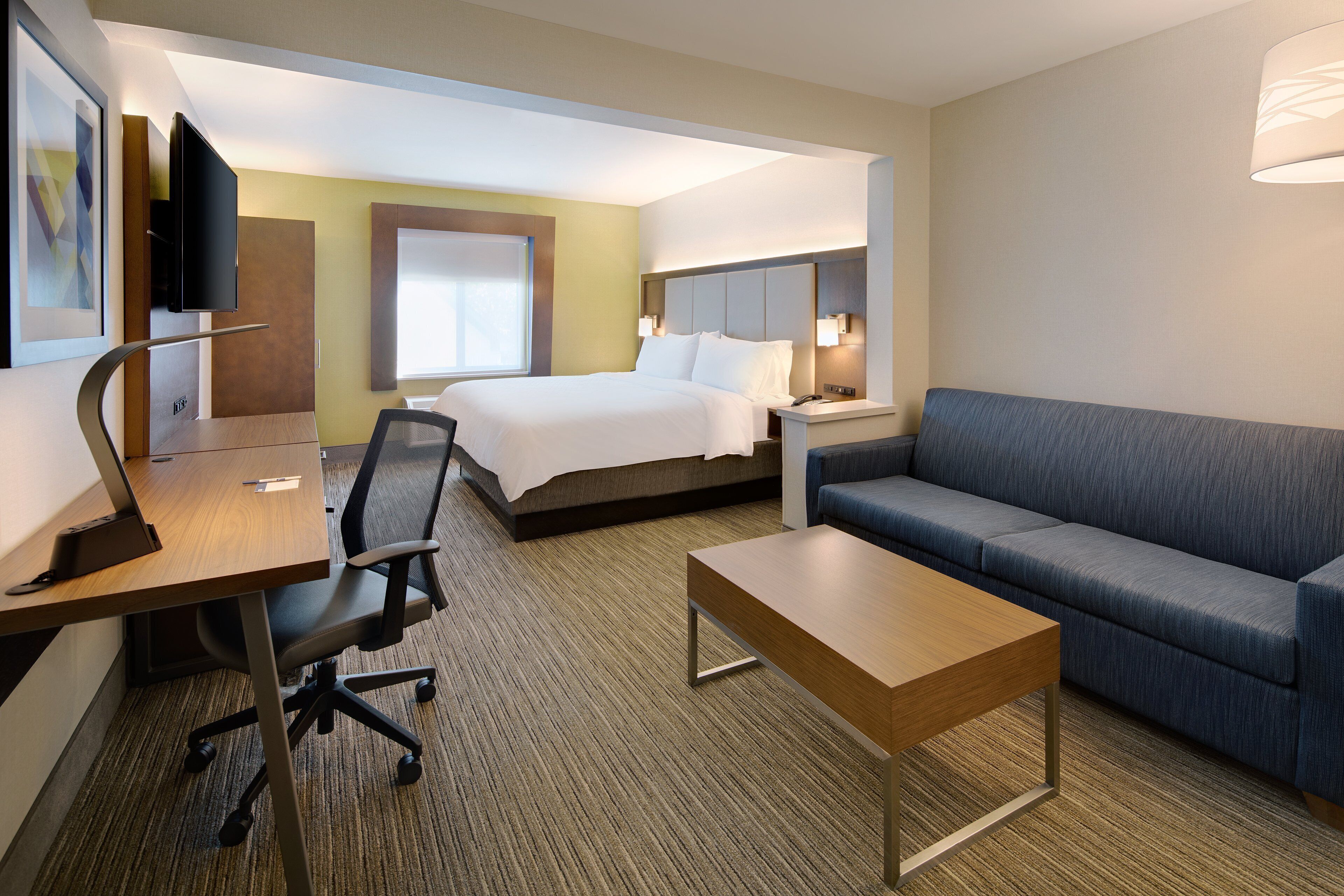 A hotel room with a bed, a desk with a chair, a sofa, and a bedside table.