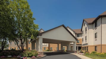 A multi-story hotel with a covered entrance, a landscaped driveway, and a clear blue sky.