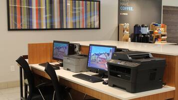 Una recepción con múltiples monitores de computadora, una impresora y una estación de café al fondo.