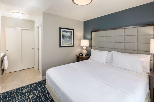 A hotel room with a large bed, a nightstand with a lamp, a framed picture on the wall, and a door leading to a bathroom.