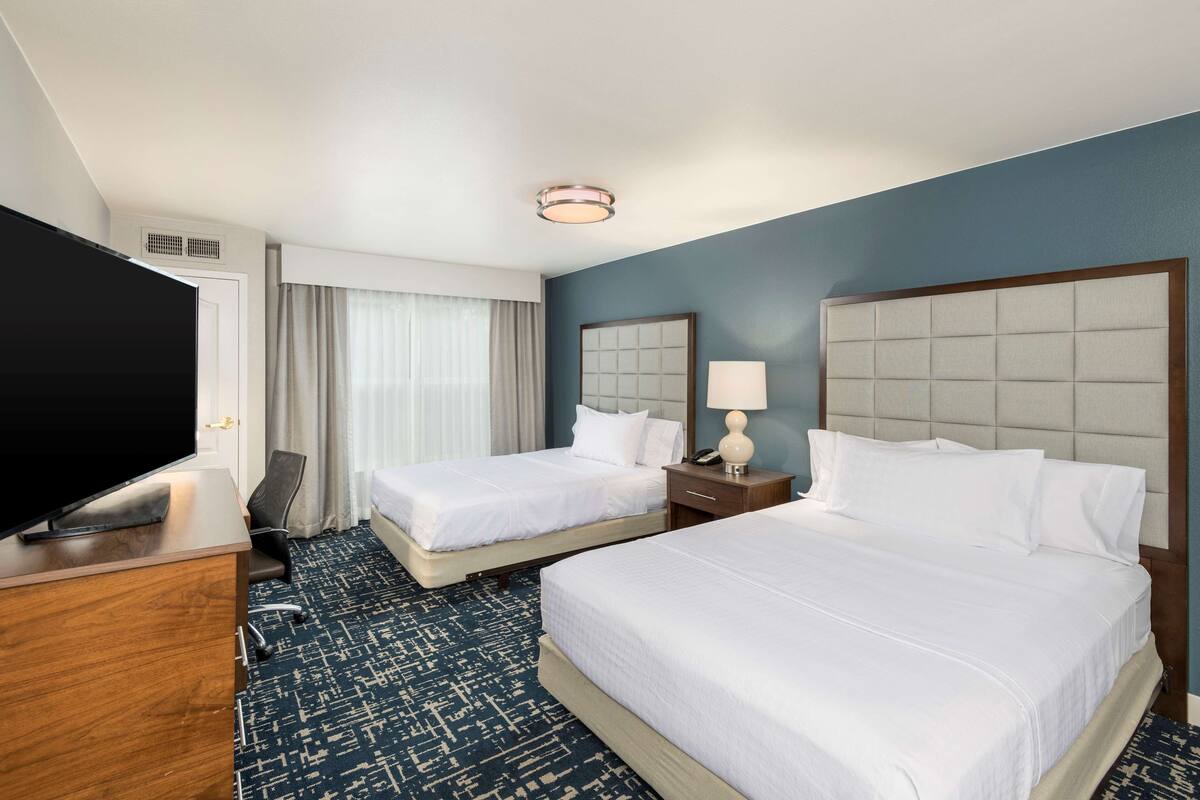 Una habitación de hotel con dos camas, televisión, escritorio y un espejo grande.