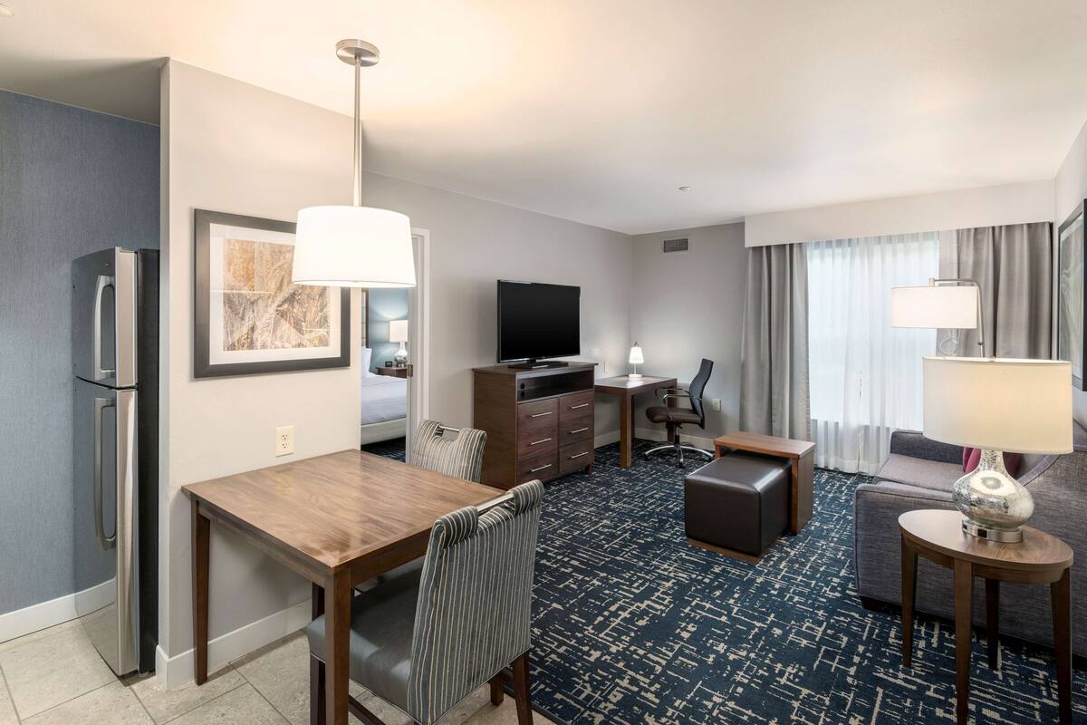 Habitación de hotel con comedor, sofá, televisor y minibar.