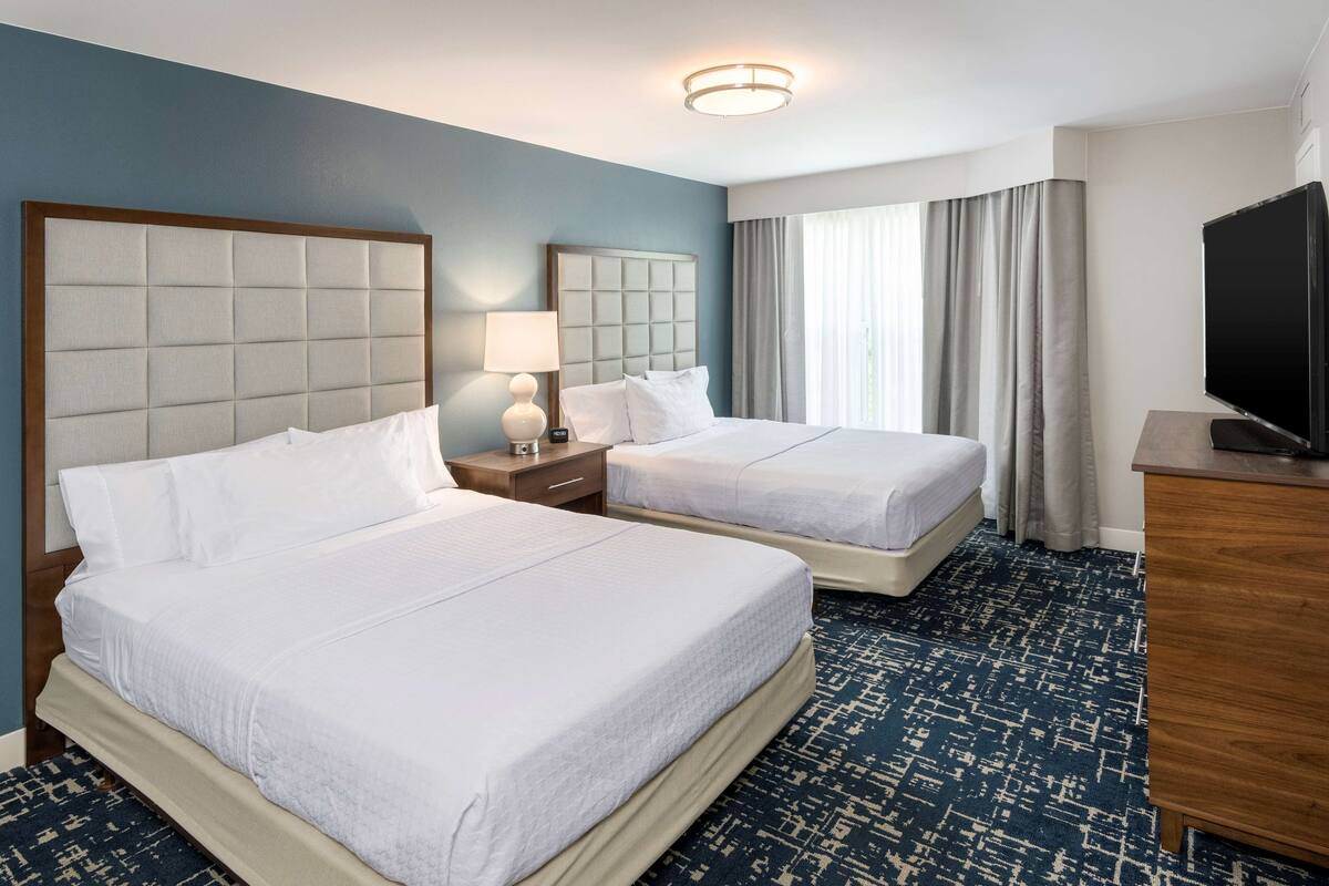 Habitación de hotel con dos camas, televisión, escritorio y ventana con cortinas.