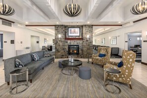 A spacious lobby with a stone fireplace, comfortable seating, and a modern chandelier.