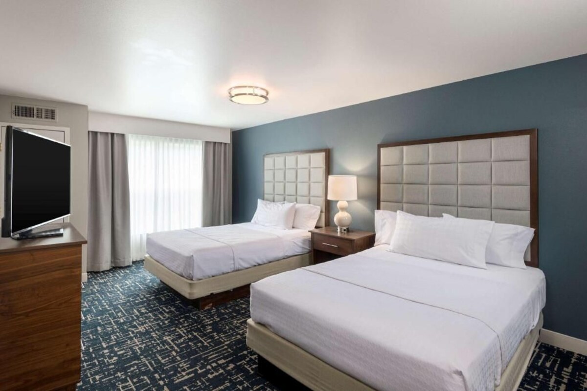 A hotel room with two beds, a TV, a desk, and a window with curtains.