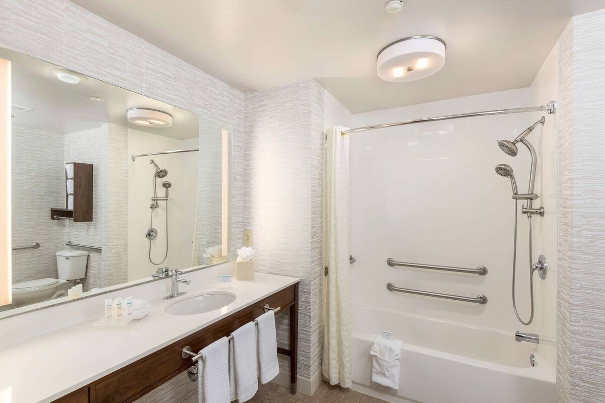 Un baño moderno con un espejo grande, un lavamanos, una bañera y una ducha.