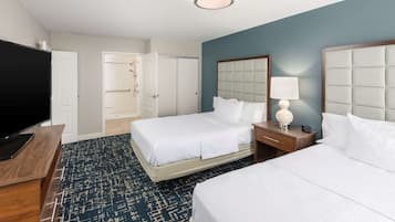 A hotel room with two beds, a TV, a desk, and a bathroom with a shower and toilet.