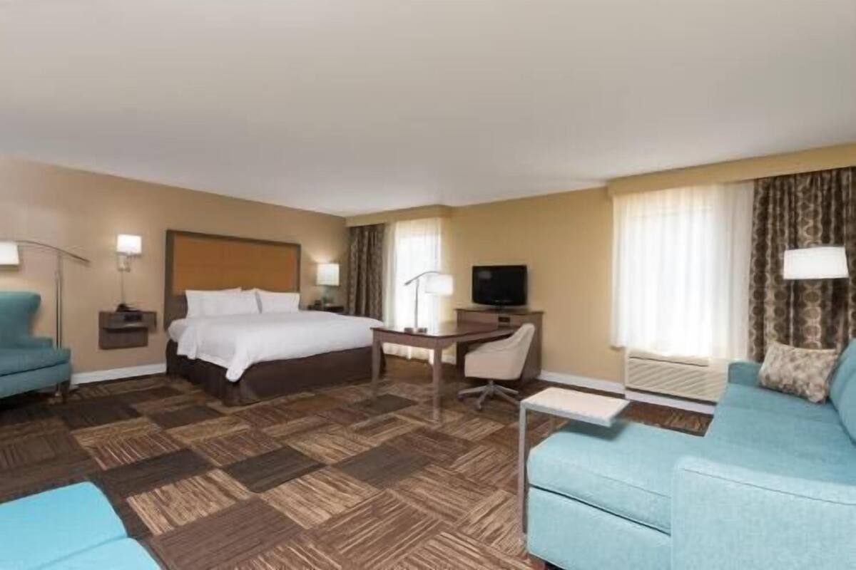 A hotel room with a bed, a desk, a television, a chair, and two armchairs.