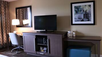 A hotel room with a desk, a television, a chair, a microwave, and a small cabinet.