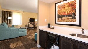 A hotel room with a kitchenette, a sofa, a TV, and a framed picture of autumn leaves on the wall. - Hampton Inn & Suites Fremont (Fremont)