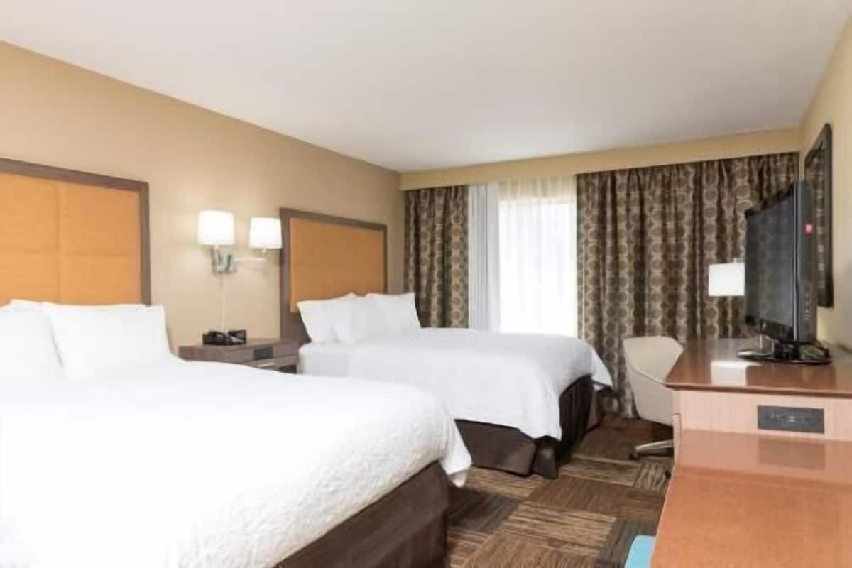 A hotel room with two beds, a desk, a television, and a window with curtains.
