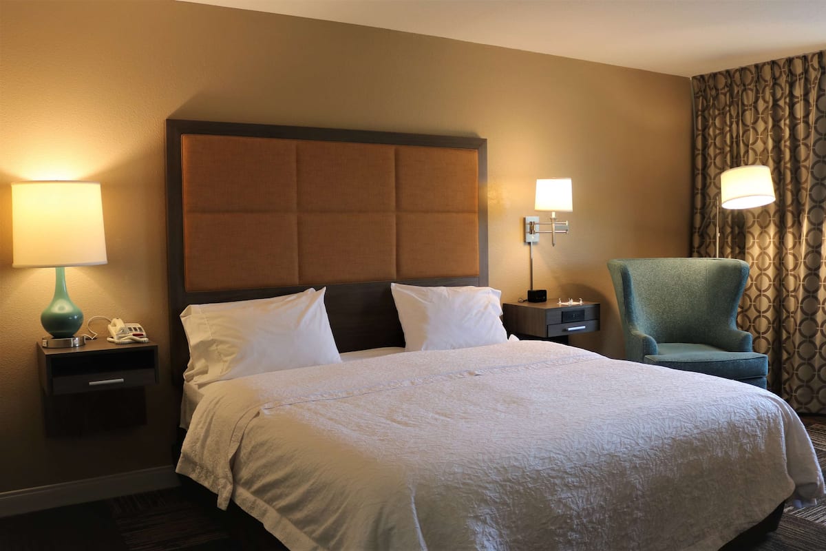 A hotel room with a large bed, two bedside tables, a chair, and a lamp.