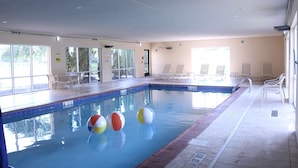 An indoor swimming pool with clear glass walls, a tiled edge, and three beach balls floating in the water. - Hampton Inn & Suites Fremont (Fremont)