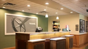 A reception desk with a large 'travel' sign, a counter, and a view of the lobby area. - Hampton Inn & Suites Fremont (Fremont)