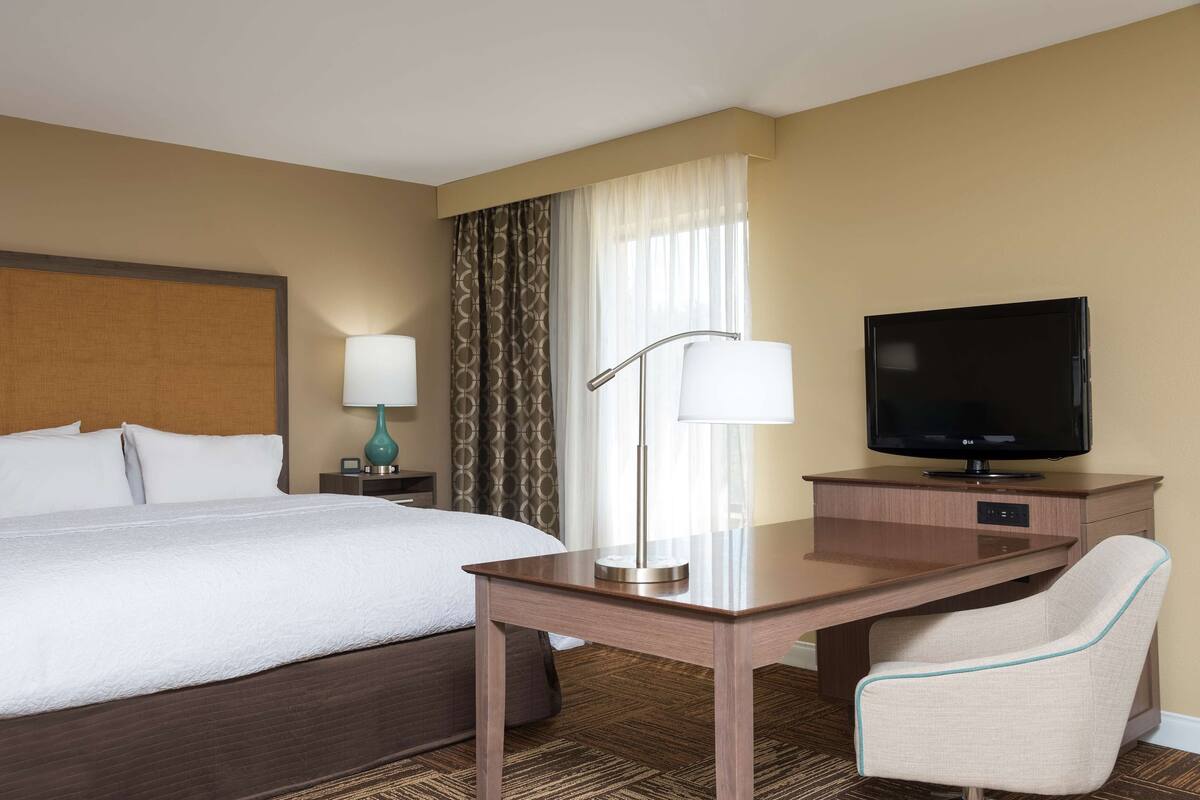 A hotel room with a large bed, a desk with a chair, a television, and a lamp.