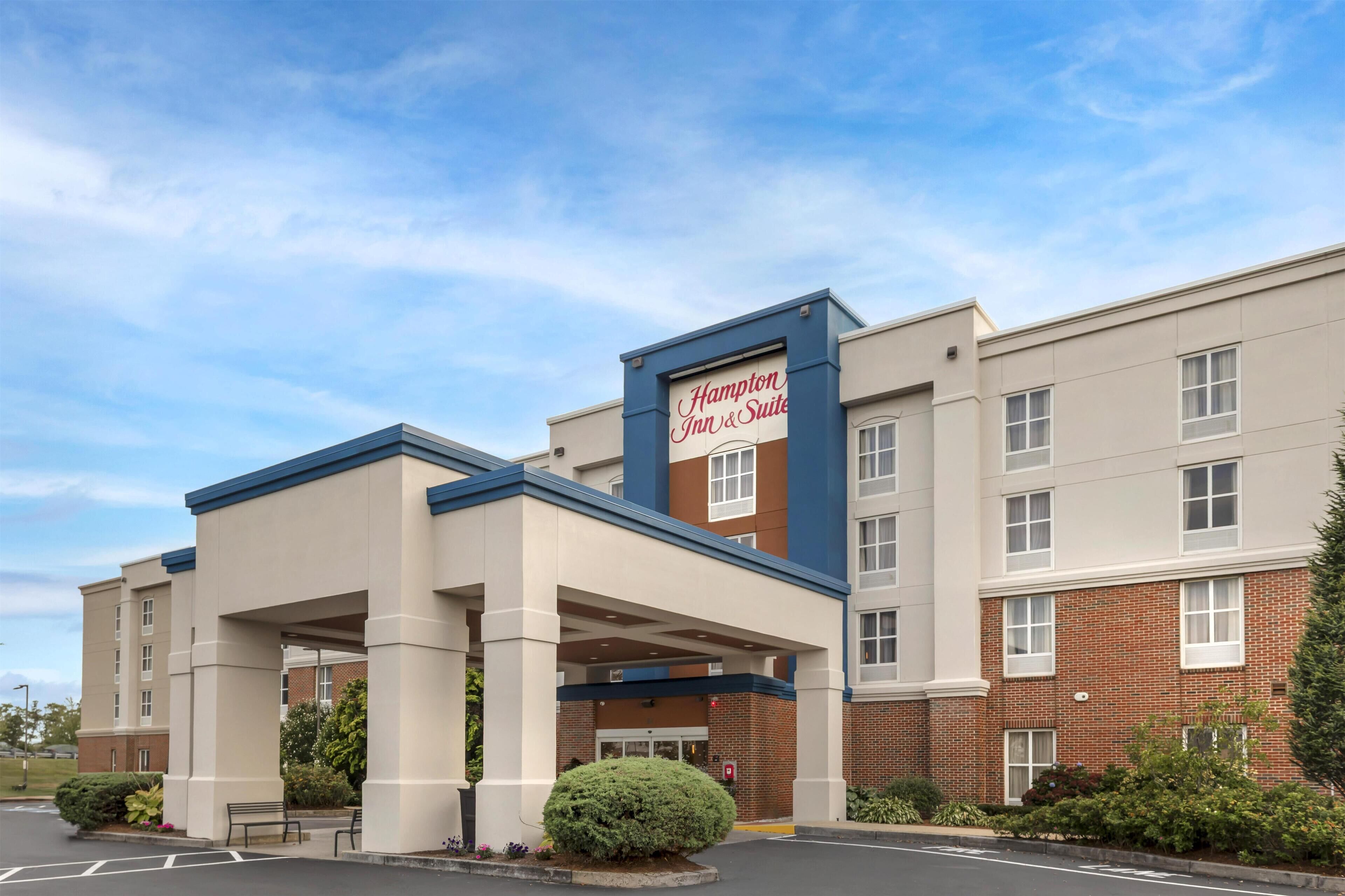 A Hampton Inn & Suites hotel with a covered entrance, brick facade, and a sign above the entrance.