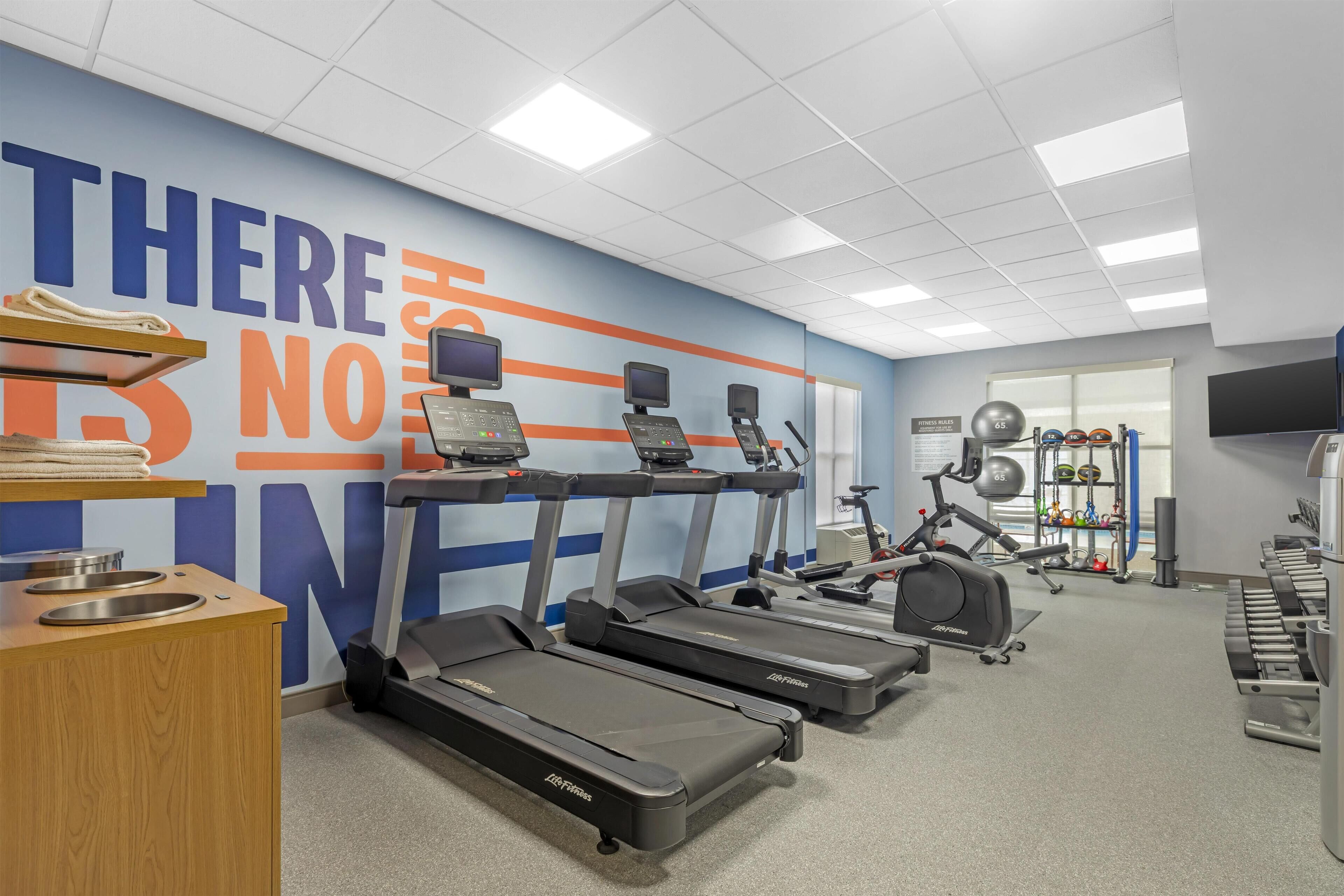 Un gimnasio con cintas de correr, una pared con letrero motivacional y un soporte para pesas.