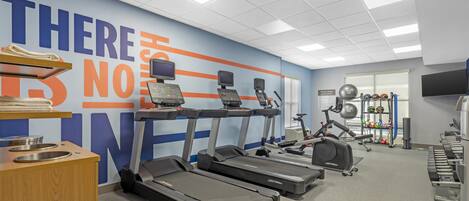 Un gimnasio con cintas de correr, una pared con letrero motivacional y un soporte para pesas.