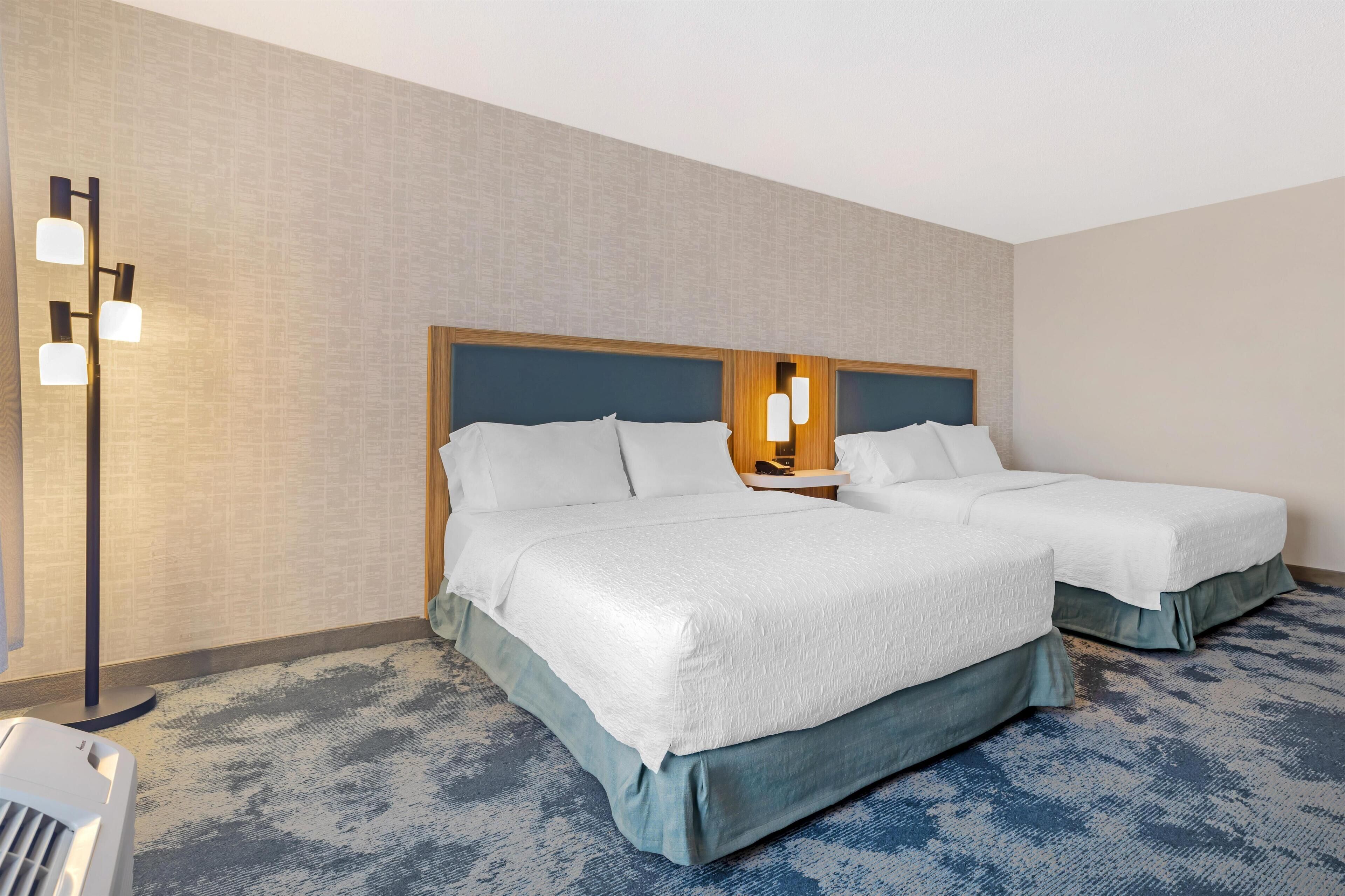 Une chambre d’hôtel avec deux lits, une grande fenêtre, un lampadaire et un sol recouvert de moquette.