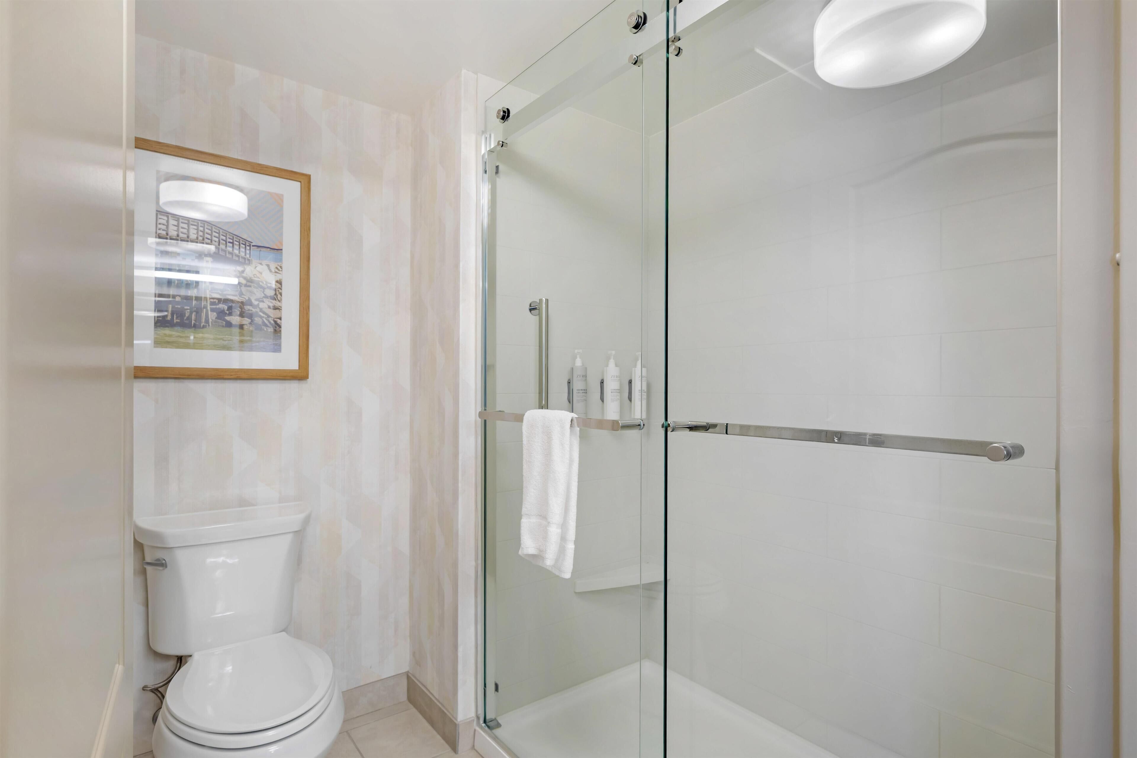 Ein modernes Badezimmer mit einer in Glas abgeschirmten Dusche, einer Toilette und einem gerahmten Bild an der Wand.