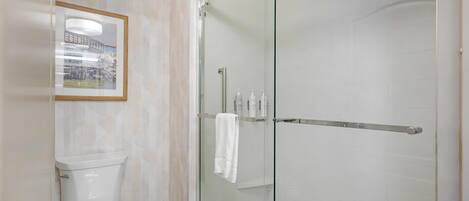 Ein modernes Badezimmer mit einer in Glas abgeschirmten Dusche, einer Toilette und einem gerahmten Bild an der Wand.