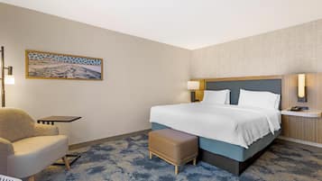 Una habitación de hotel con cama, una silla, una mesita, un banco y una lámpara fijada a la pared.