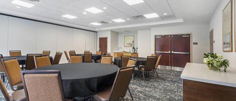 A conference room with a large round table, multiple chairs, a reception desk, and a carpeted floor.