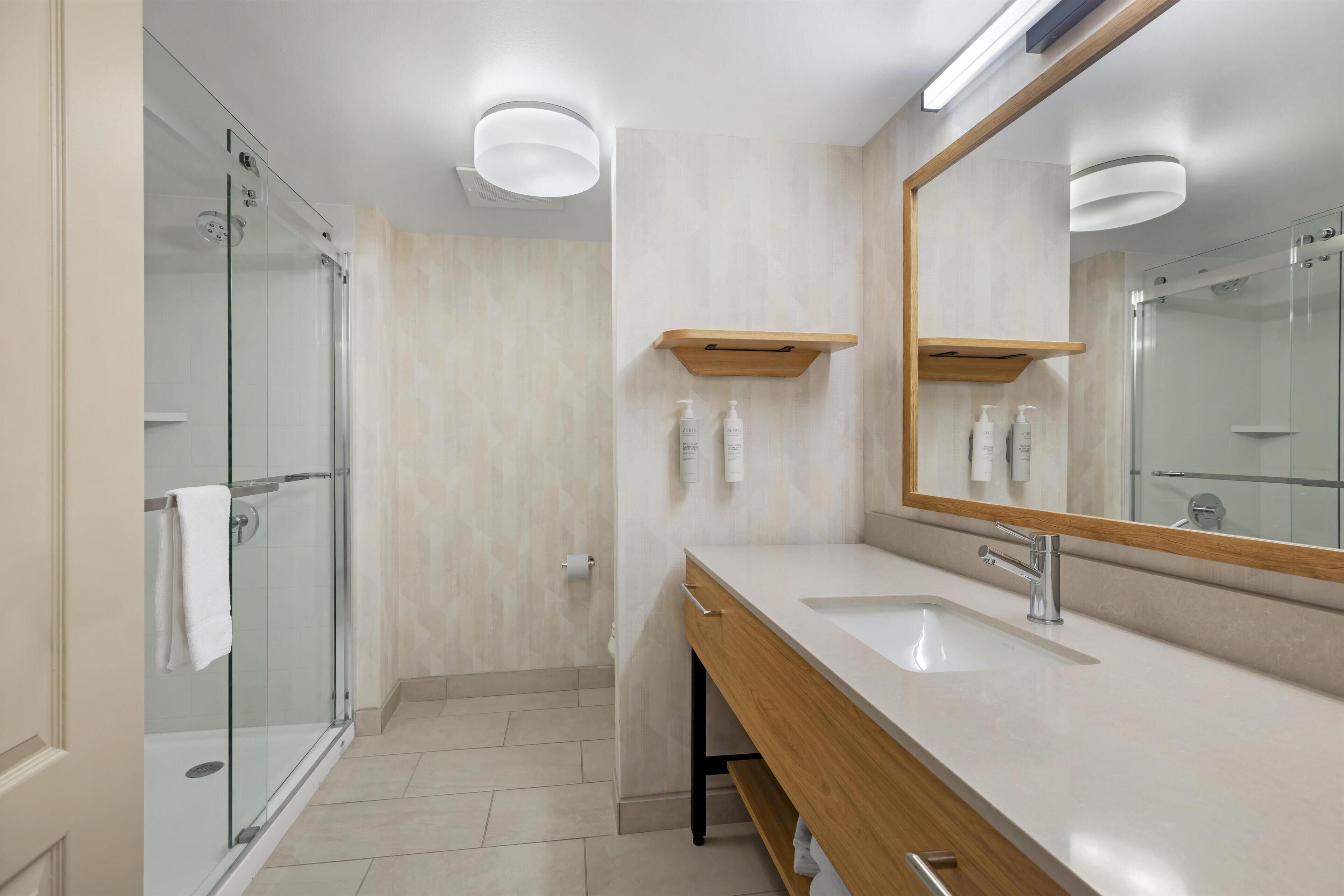 Een moderne badkamer met een glazen douchecabine, een houten wastafelmeubel met een wastafel en een spiegel met houten lijst.