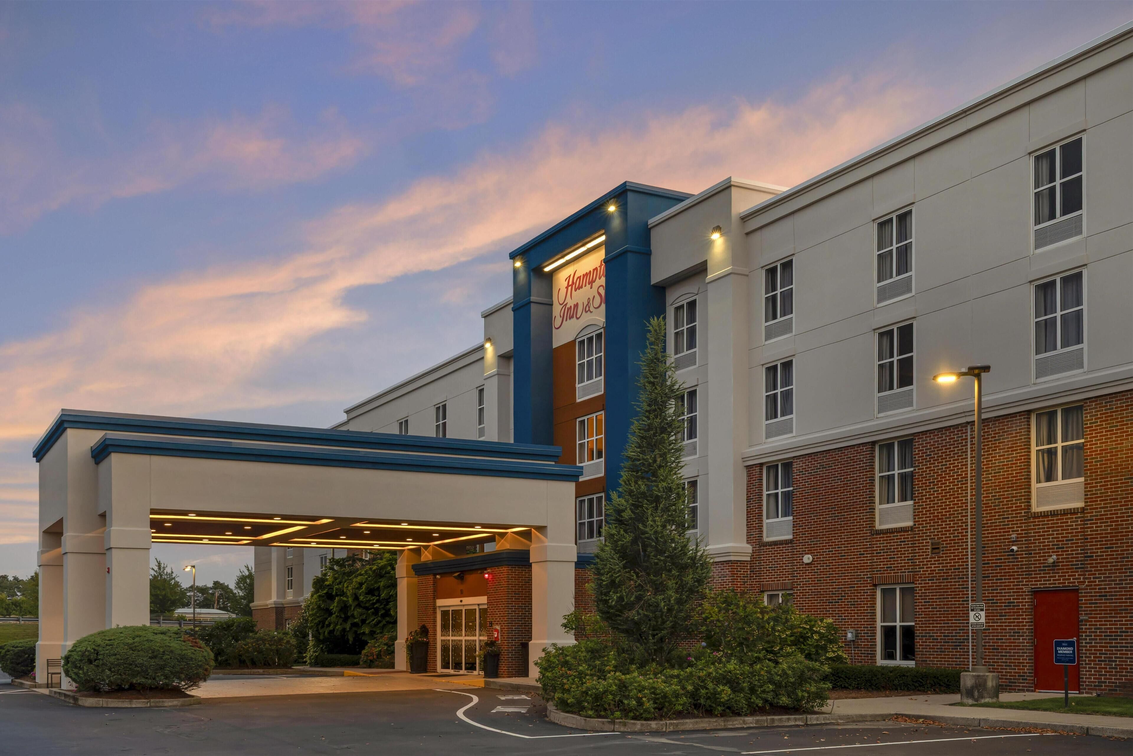 Entrada de un hotel con un vestíbulo techado, un letrero de Hampton Inn & Suites y fachada de ladrillo.