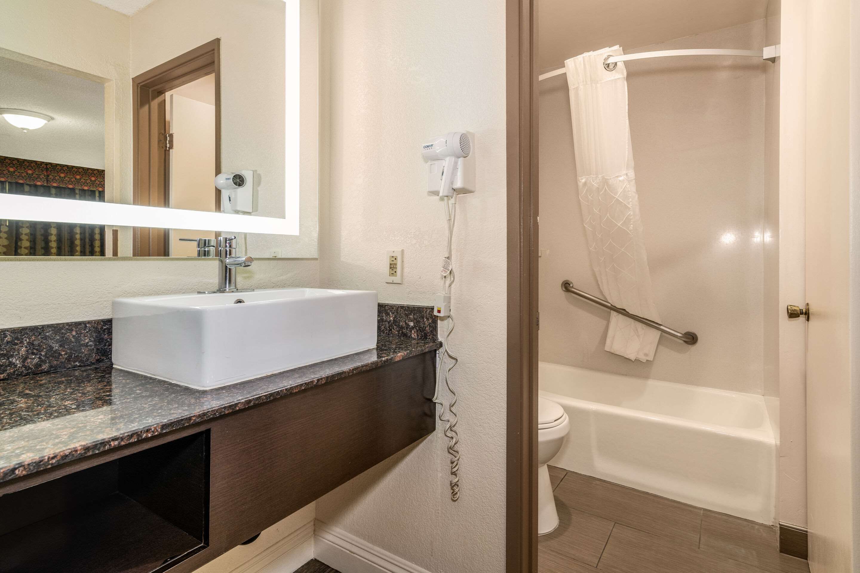 Un baño con un lavamanos blanco, un secador de pelo montado en la pared, una ducha con puerta de vidrio y un perchero para toallas.