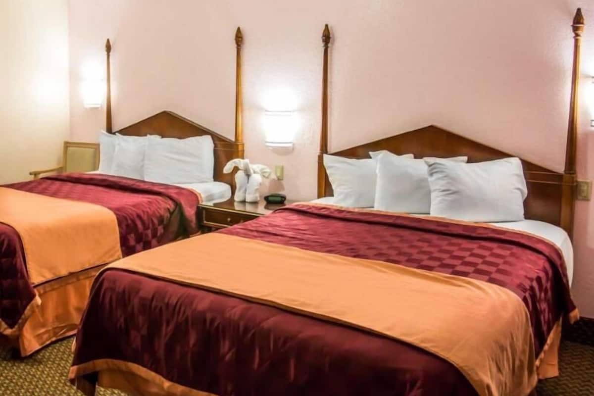 A hotel room with two beds, each with a wooden headboard, a nightstand, a lamp, and a small statue.