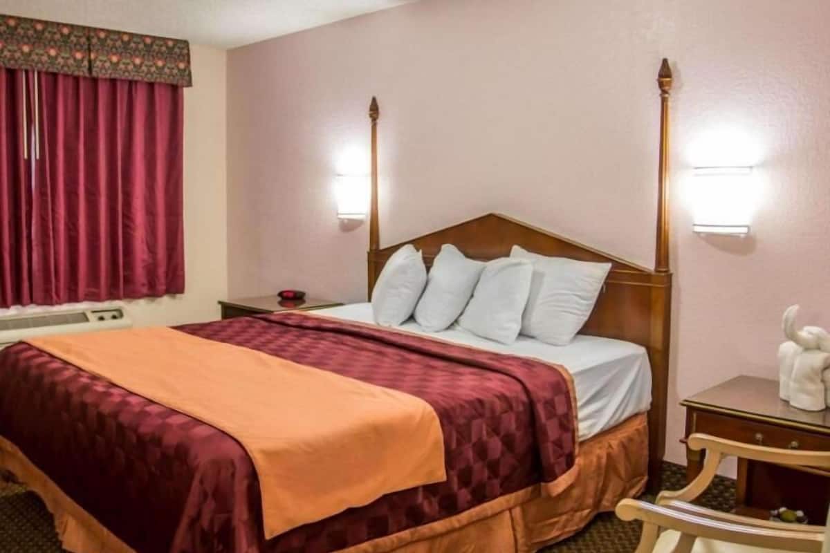 A hotel room with a four-poster bed, a bedside table with a lamp, and a nightstand with a red object.