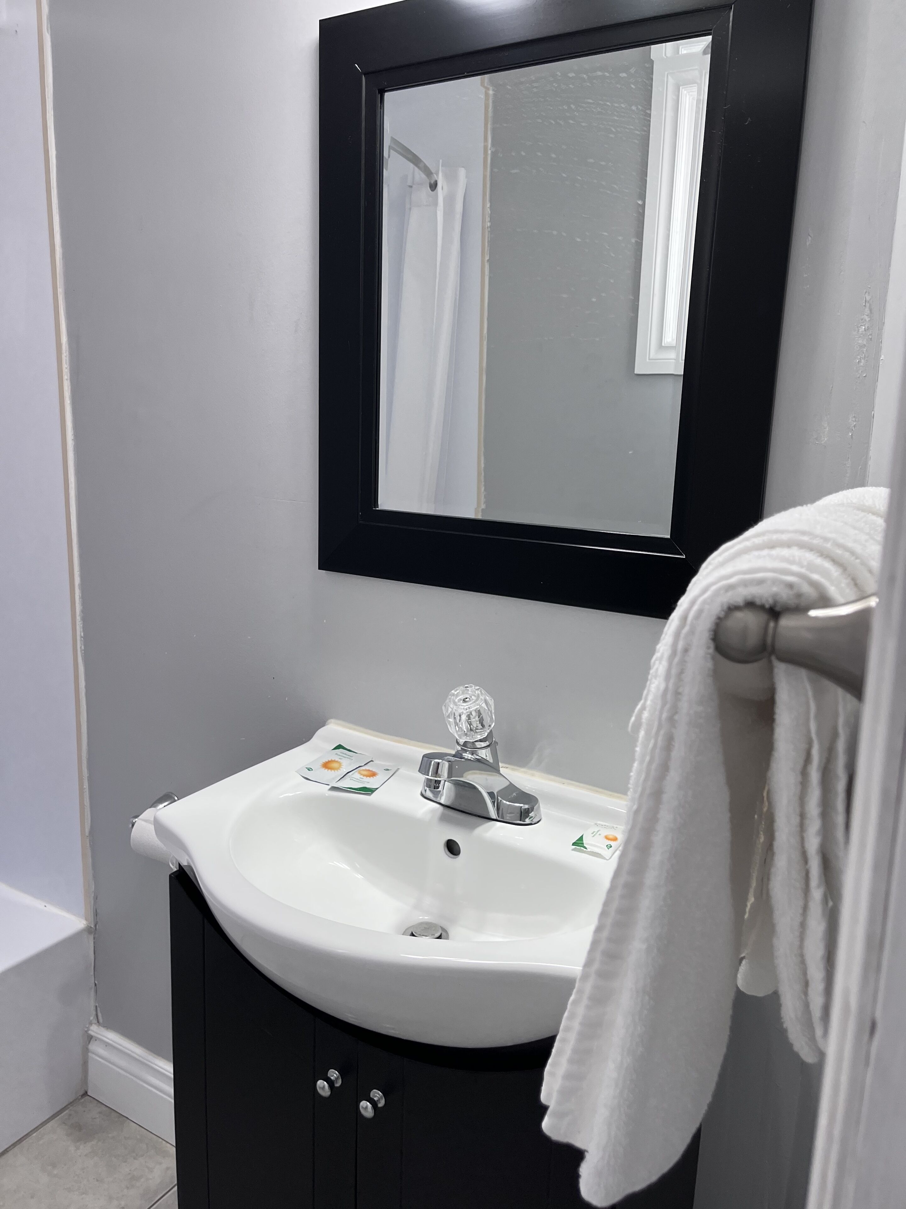 A bathroom with a white sink, black cabinet, and a mirror with a black frame.