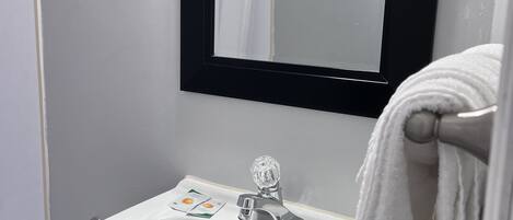 Un baño con lavamanos blanco, mueble negro y espejo con marco negro.