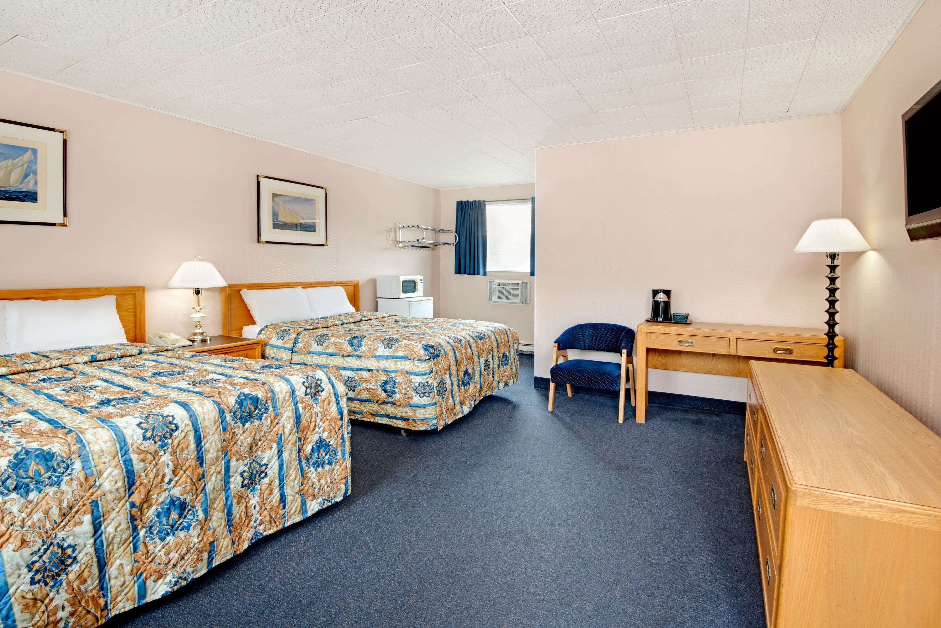 A hotel room with two beds, a desk, a chair, a TV, and a microwave.