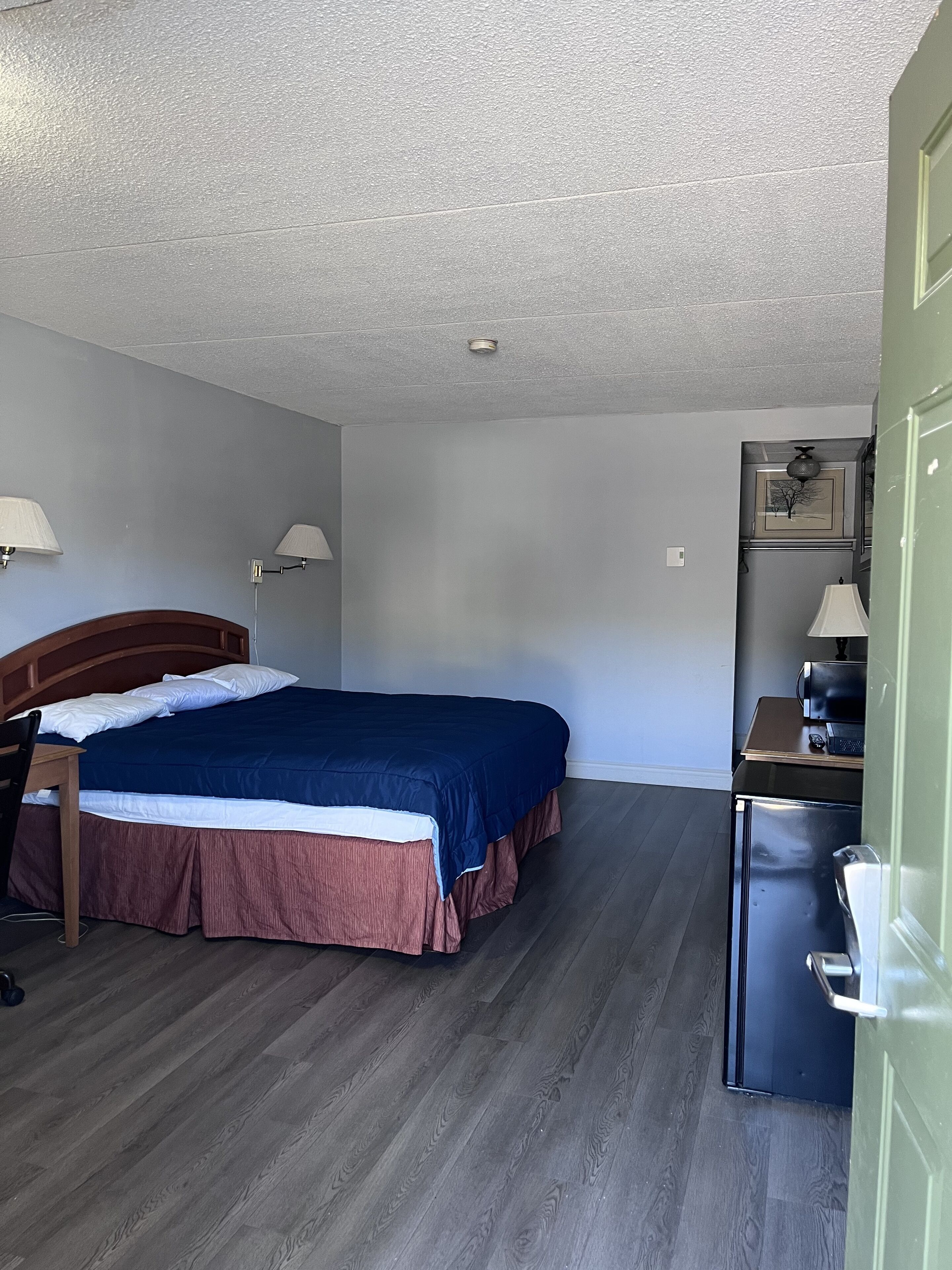 A bedroom with a bed, a desk, a chair, and a refrigerator.