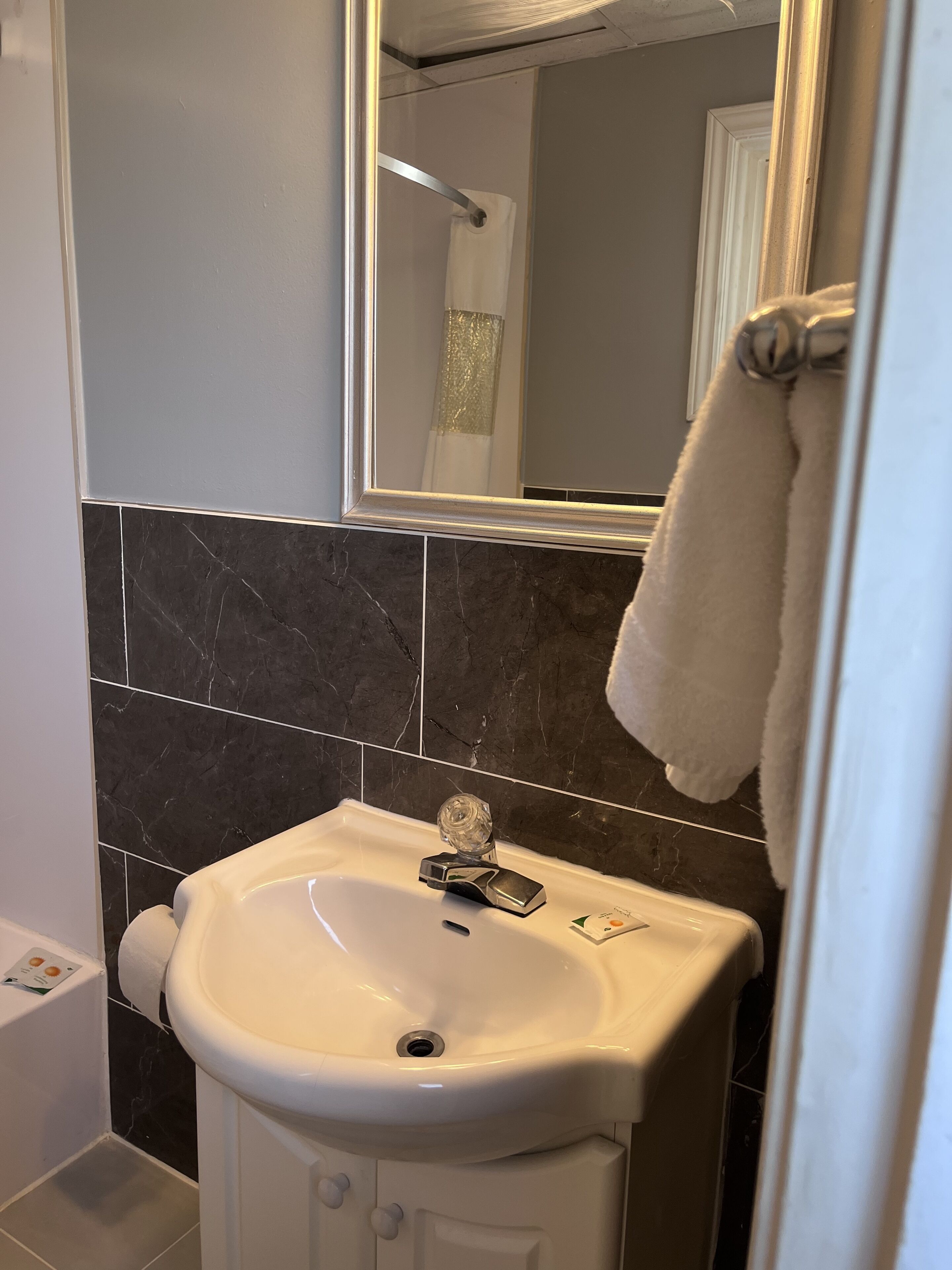 A bathroom with a white sink, dark marble tiles, a mirror, and a towel hanging on the wall.