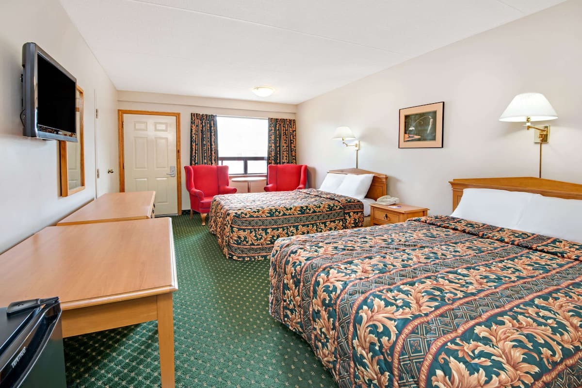 A hotel room with two beds, a desk, a TV, a window with curtains, and a painting on the wall.