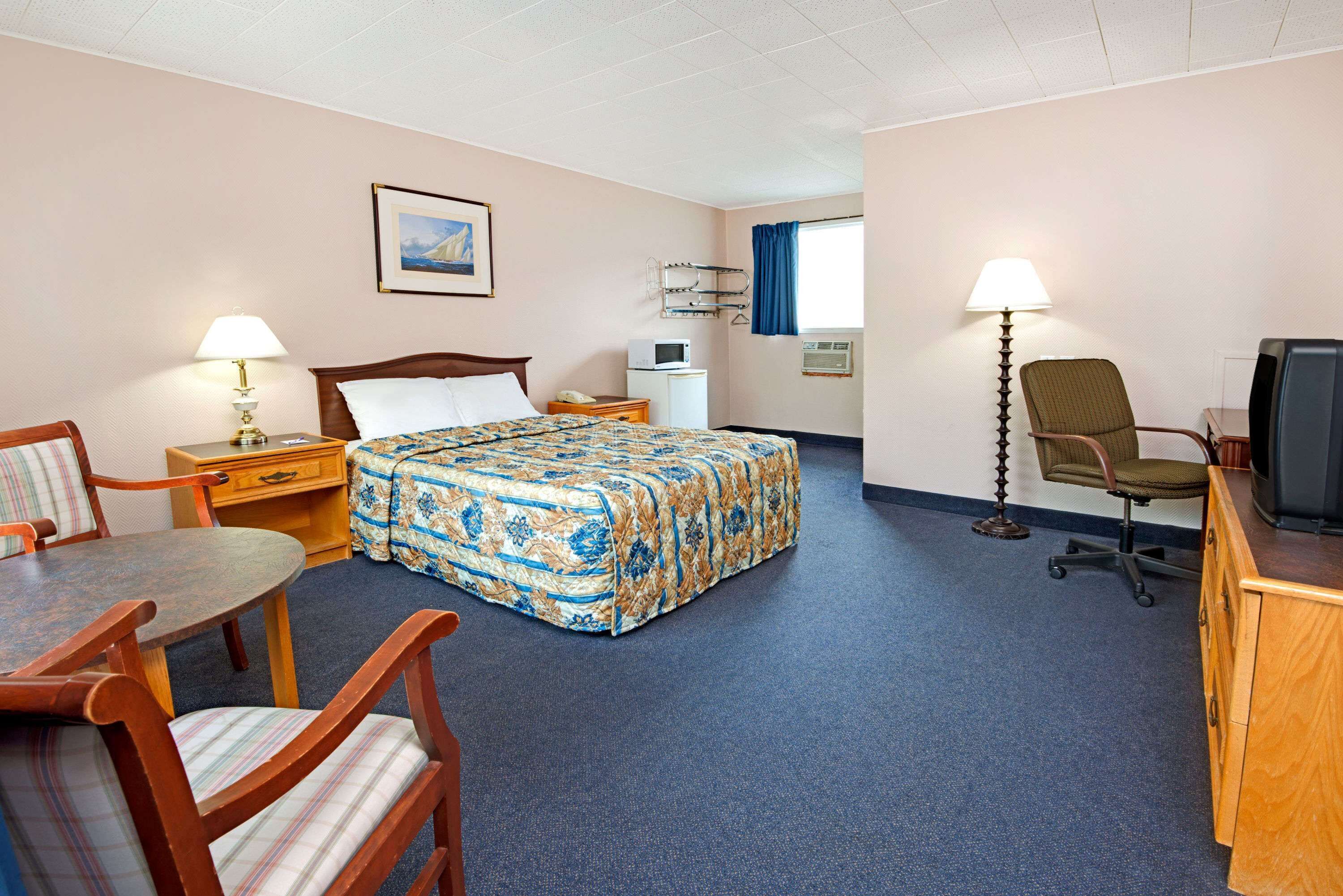A hotel room with a bed, a desk, a chair, a television, and a lamp.