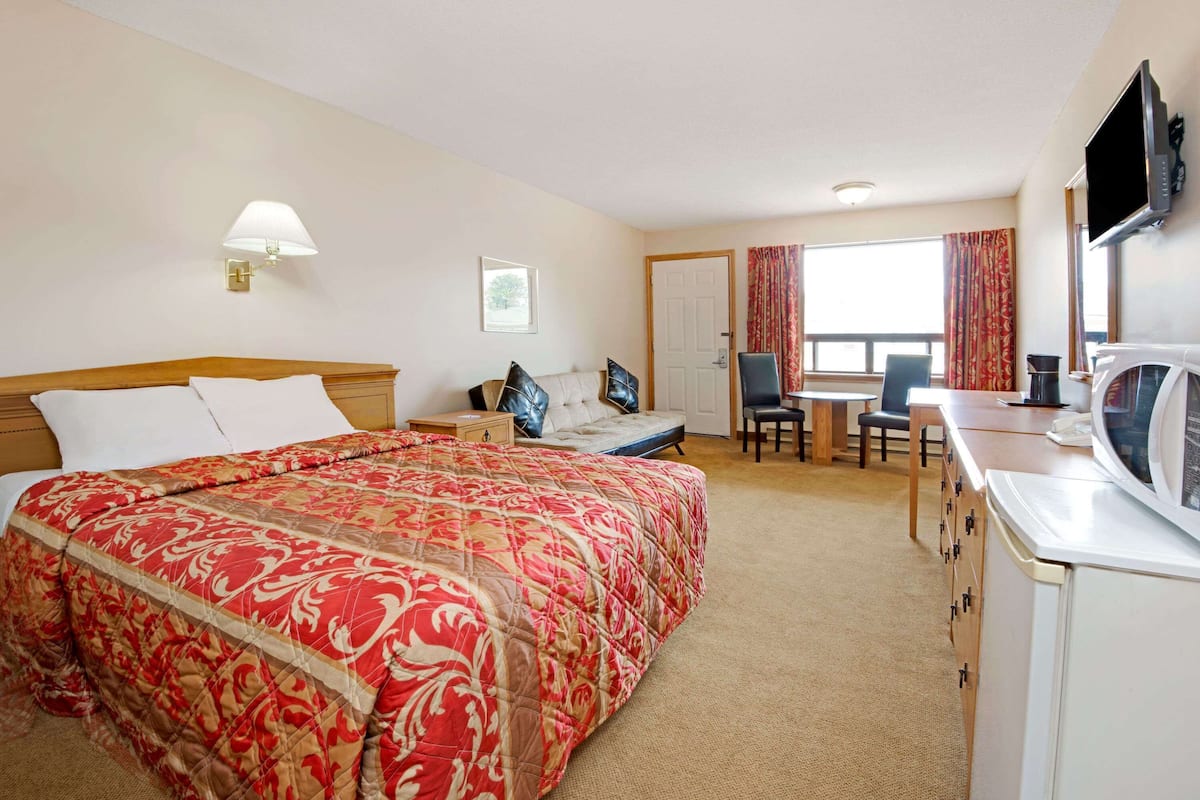 A hotel room with a large bed, a desk, a chair, a television, and a wardrobe.