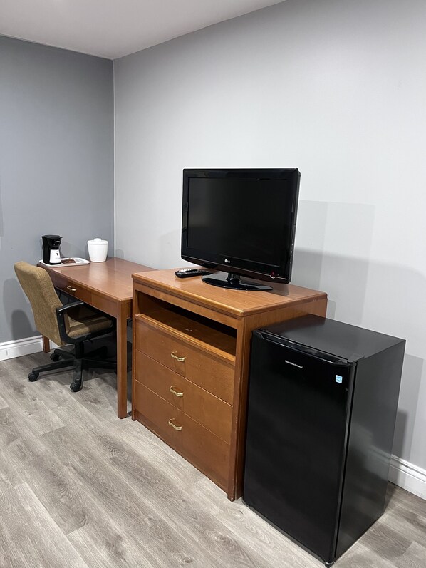 Un espacio de oficina compacto con un escritorio de madera, un monitor negro, un refrigerador pequeño negro y una silla.
